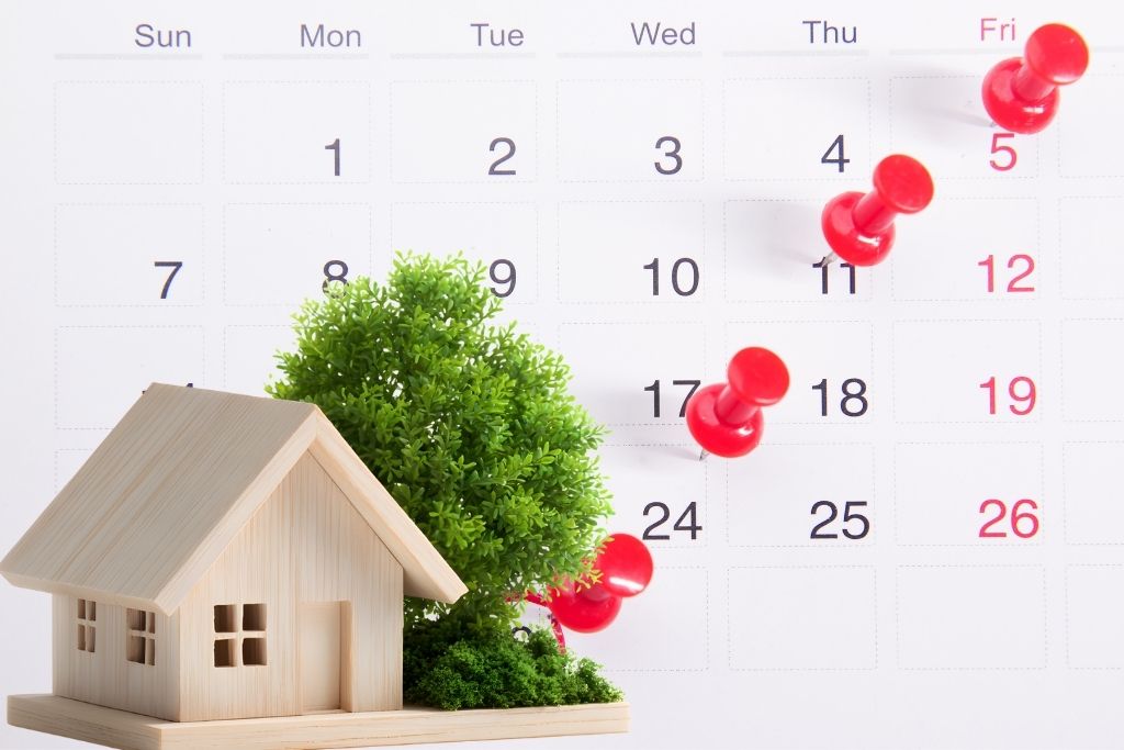Calendar dates pinned next to a miniature house, representing a home closing schedule.
